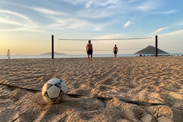 Quadra de futevôlei na areia com a bola perto da linha de fundo e a rede ao fundo