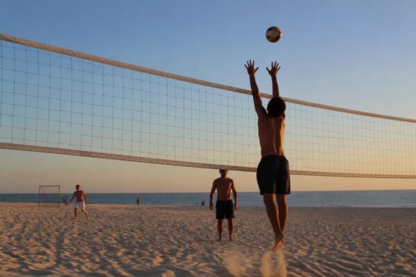 Bloqueador de costas com as mãos acima da rede de vôlei de praia, bola no ar e luz de fim de tarde