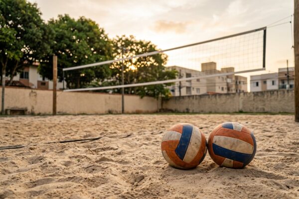 Duas bolas na areia de uma arena, com a rede ao fundo ao entardecer
