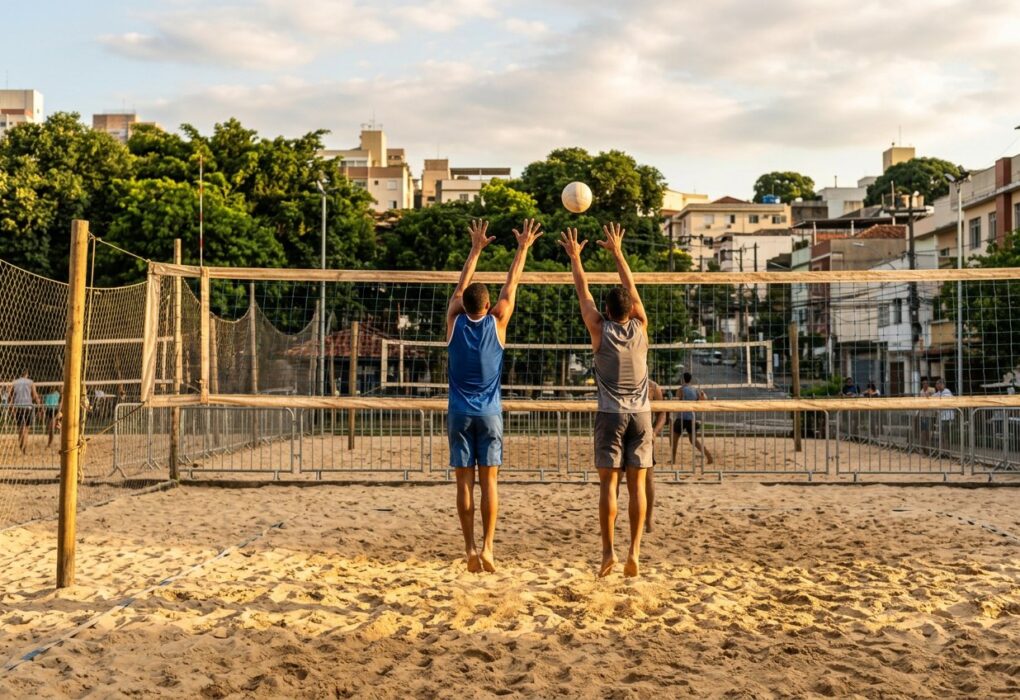 Dois jogadores de costas junto à rede de uma arena de vôlei de praia ao fim da tarde