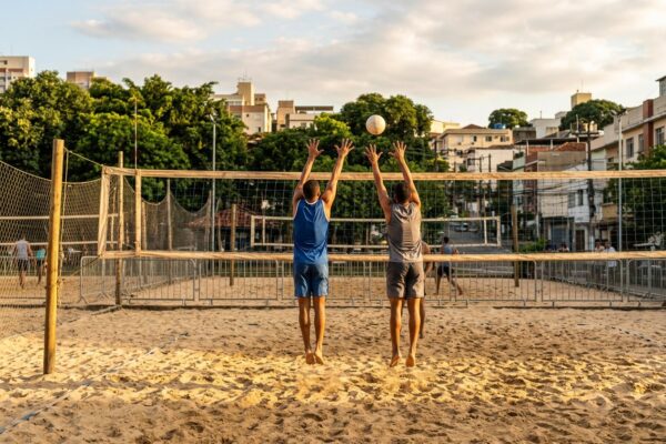 Dois jogadores de costas junto à rede de uma arena de vôlei de praia ao fim da tarde